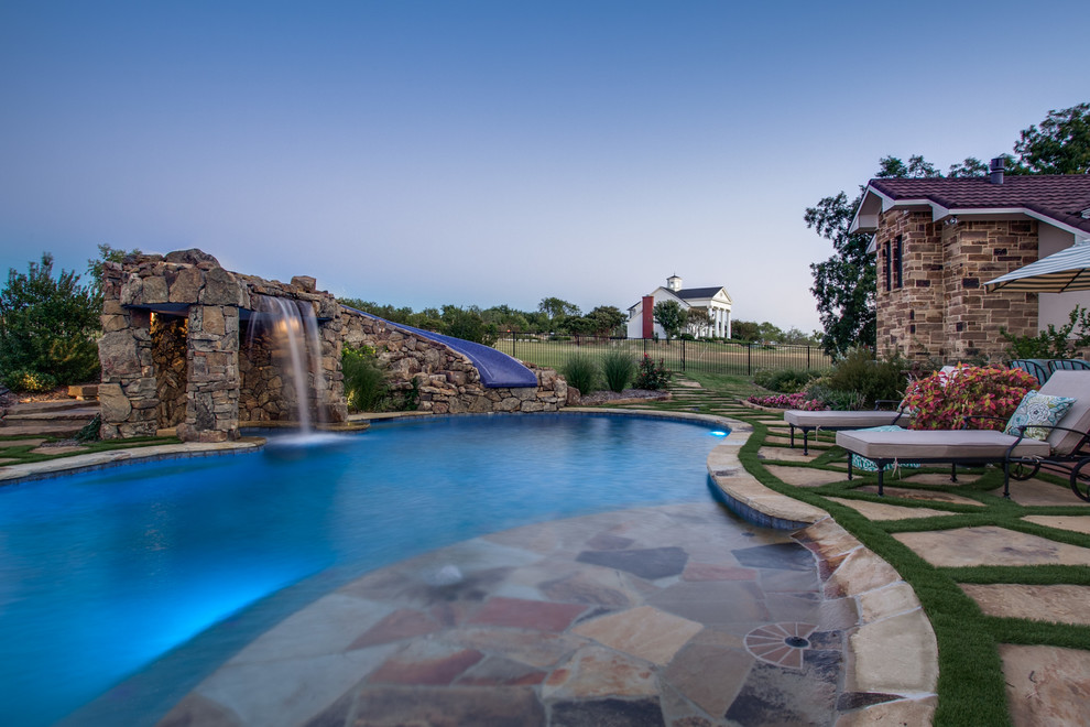 Inspiration for a country backyard custom-shaped pool in Dallas with a water feature and natural stone pavers.