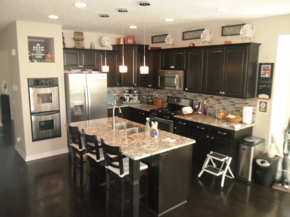 This is an example of a mid-sized transitional l-shaped eat-in kitchen in Columbus with an undermount sink, recessed-panel cabinets, dark wood cabinets, granite benchtops, metallic splashback, glass sheet splashback, stainless steel appliances, dark hardwood floors and with island.