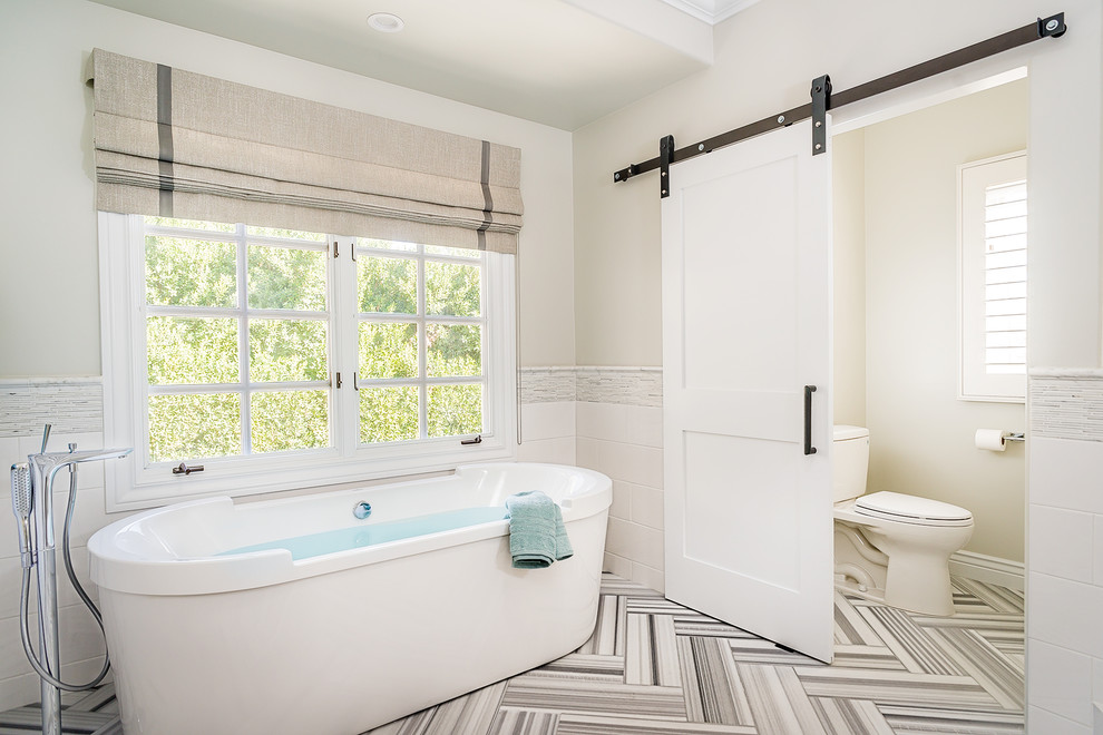 Photo of a large transitional master bathroom in Los Angeles with a freestanding tub, marble floors, a two-piece toilet, white tile and beige walls.