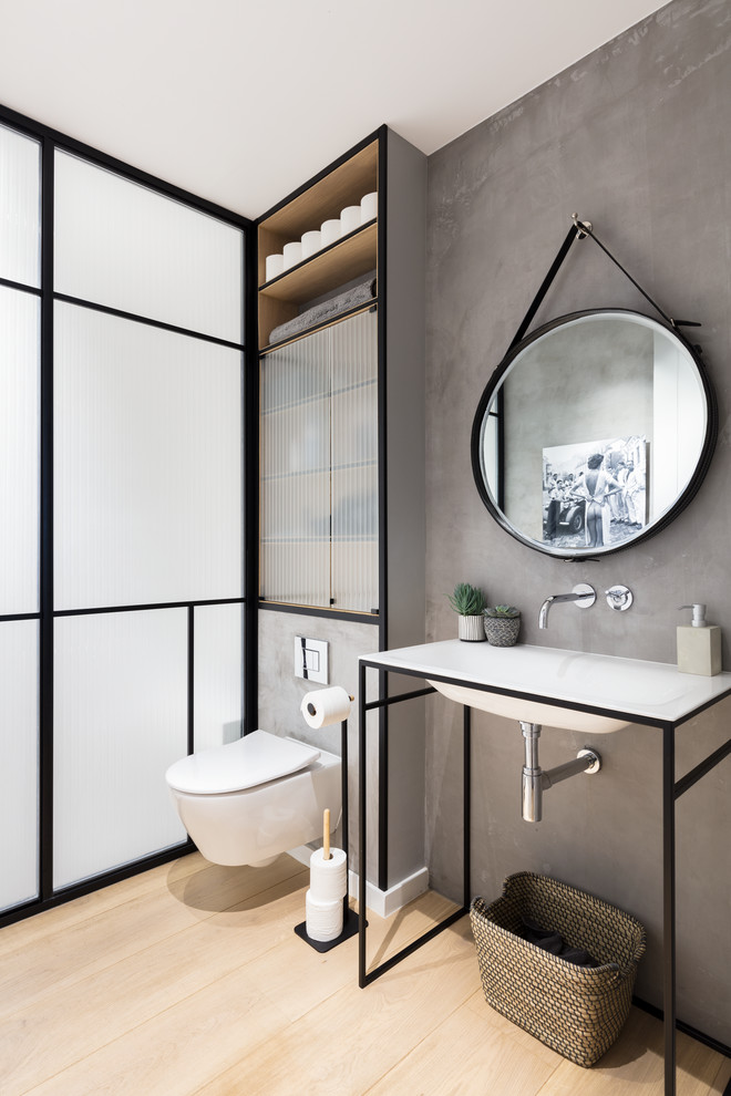 This is an example of a contemporary powder room in London with a wall-mount toilet, grey walls, light hardwood floors, an integrated sink, glass-front cabinets and beige floor.