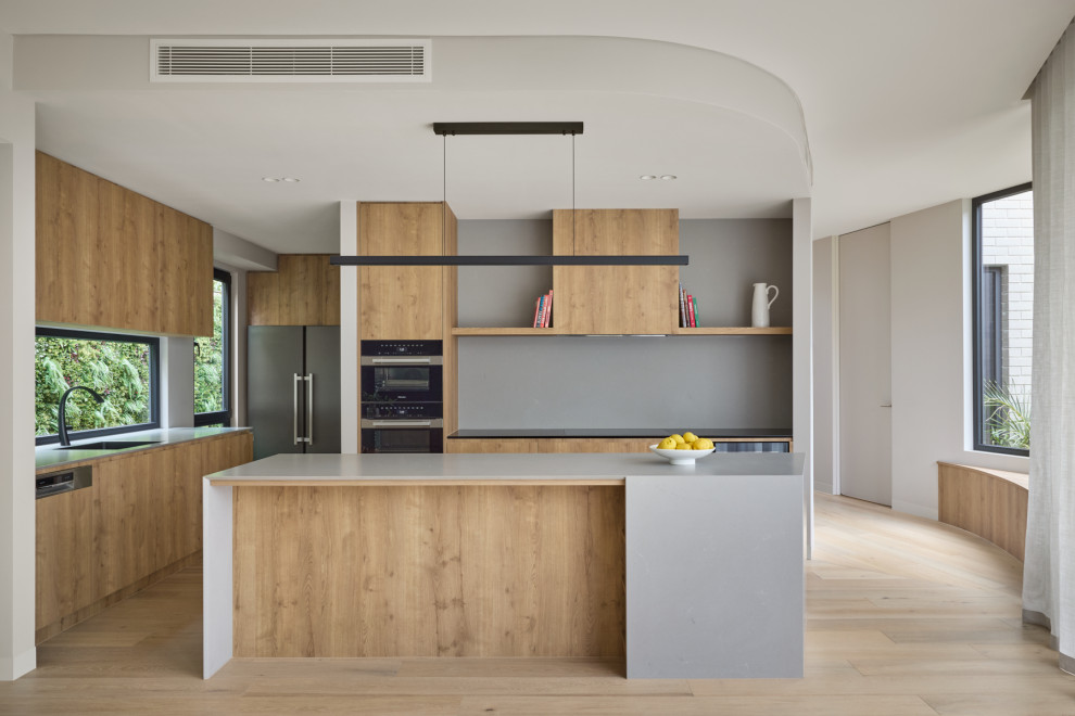 Design ideas for a mid-sized contemporary open plan kitchen in Melbourne with flat-panel cabinets, light wood cabinets, concrete benchtops, grey splashback, engineered quartz splashback, black appliances, medium hardwood floors, with island and grey benchtop.