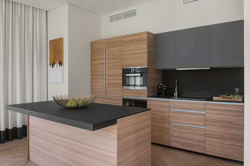 Photo of a contemporary single-wall eat-in kitchen in Moscow with flat-panel cabinets, light wood cabinets, black splashback, stainless steel appliances, light hardwood floors, with island, beige floor and black benchtop.