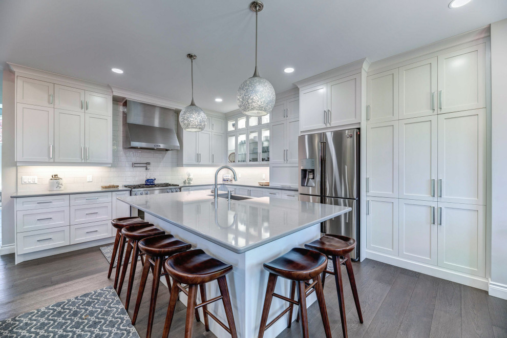 Eat-in kitchen - transitional l-shaped eat-in kitchen idea with a farmhouse sink, shaker cabinets, white cabinets, quartz countertops, stainless steel appliances, an island, white countertops and porcelain backsplash