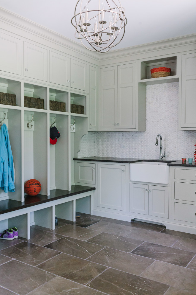 Large transitional l-shaped dedicated laundry room in Chicago with white walls, marble floors, a farmhouse sink, recessed-panel cabinets, solid surface benchtops, a concealed washer and dryer and grey cabinets.