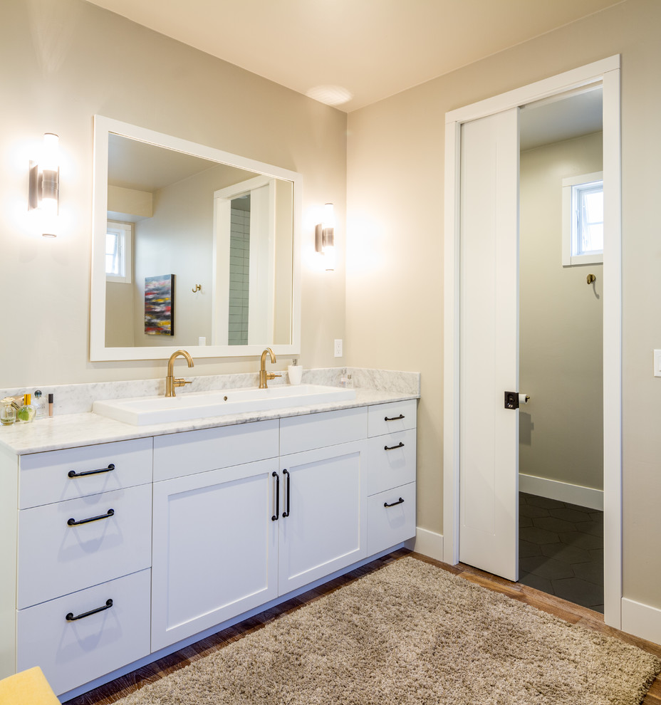Photo of a mid-sized country master bathroom in Other with shaker cabinets, white cabinets, a claw-foot tub, an alcove shower, a two-piece toilet, white tile, ceramic tile, beige walls, medium hardwood floors, a trough sink, marble benchtops, brown floor and a hinged shower door.