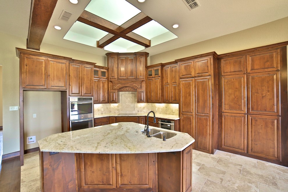 Example of a mid-sized mountain style l-shaped porcelain tile eat-in kitchen design in Dallas with an undermount sink, raised-panel cabinets, medium tone wood cabinets, granite countertops, beige backsplash, stone tile backsplash, stainless steel appliances and an island