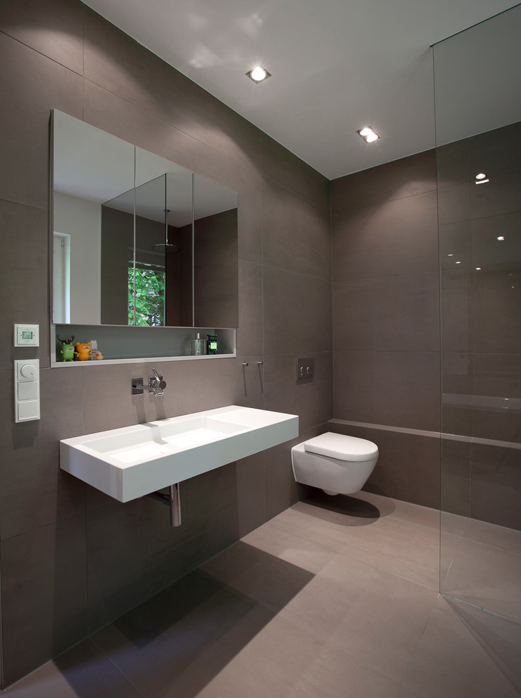 Design ideas for a mid-sized contemporary master bathroom in Frankfurt with flat-panel cabinets, a drop-in tub, a curbless shower, a wall-mount toilet, gray tile, ceramic tile, grey walls, ceramic floors and a wall-mount sink.