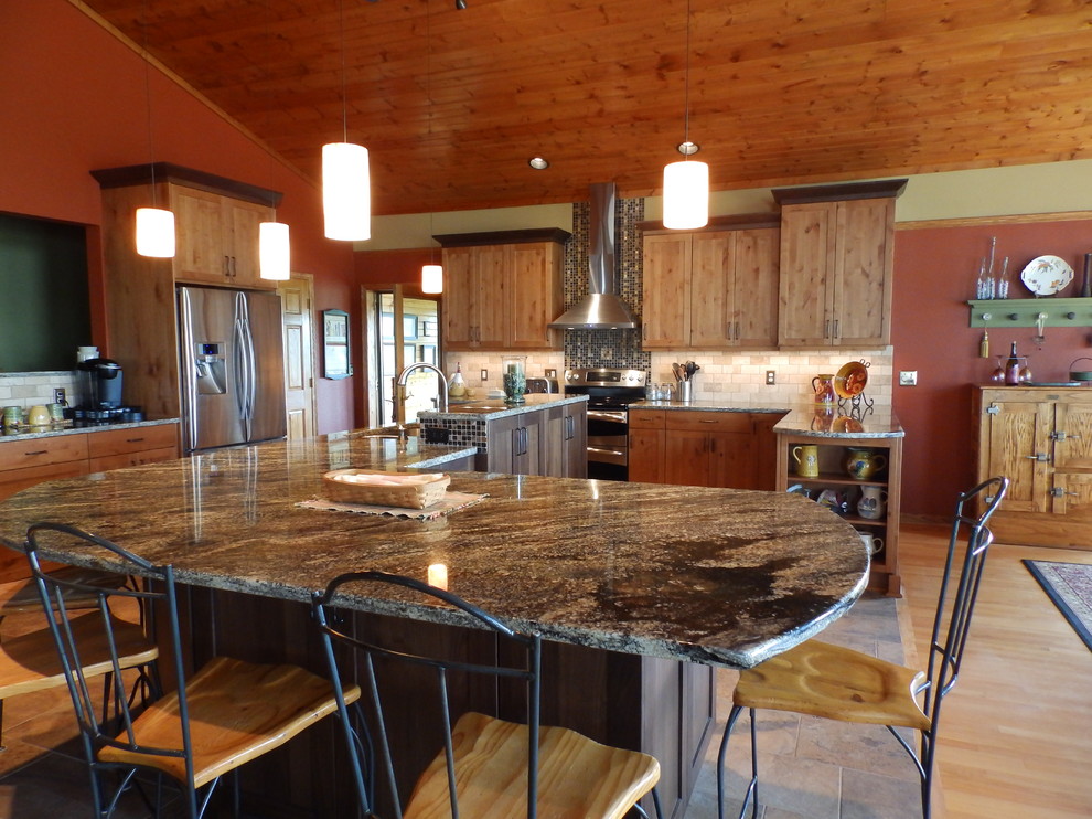 Expansive country l-shaped eat-in kitchen in Minneapolis with shaker cabinets, medium wood cabinets, granite benchtops, brown splashback, stainless steel appliances and porcelain floors.
