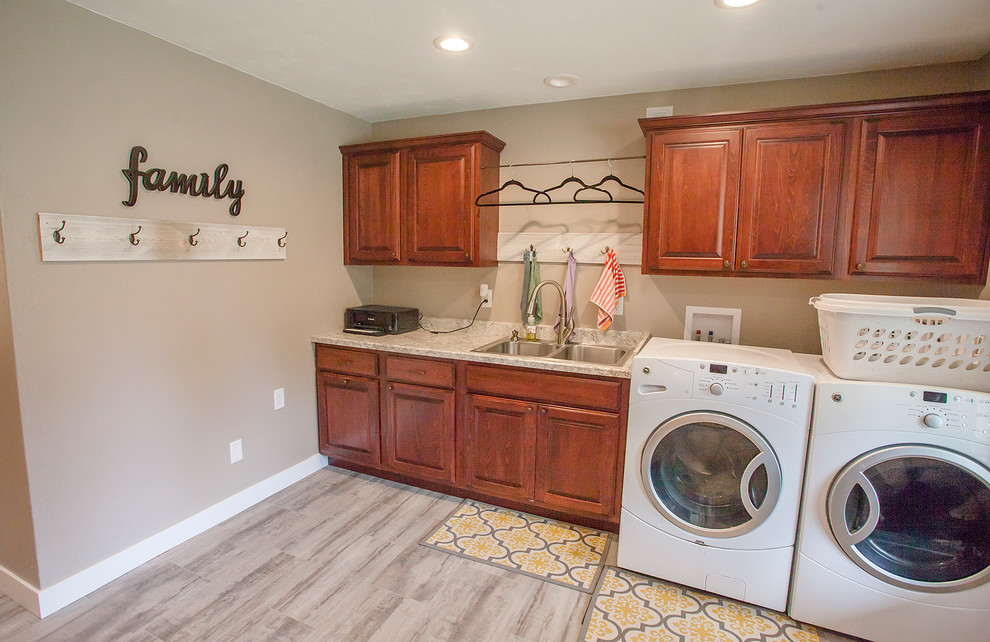 This is an example of a large country utility room in Cedar Rapids with raised-panel cabinets, red cabinets, laminate benchtops, grey walls, vinyl floors, a side-by-side washer and dryer, grey floor and beige benchtop.