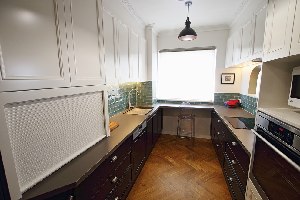 Inspiration for a mid-sized traditional galley separate kitchen in Sydney with a double-bowl sink, recessed-panel cabinets, black cabinets, tile benchtops, green splashback, ceramic splashback, stainless steel appliances, medium hardwood floors, no island, brown floor and brown benchtop.