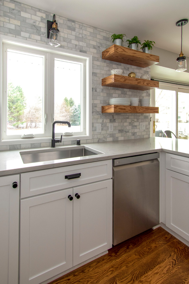 Design ideas for a mid-sized transitional u-shaped eat-in kitchen in Milwaukee with an undermount sink, shaker cabinets, white cabinets, quartz benchtops, grey splashback, marble splashback, stainless steel appliances, medium hardwood floors, a peninsula, brown floor and grey benchtop.