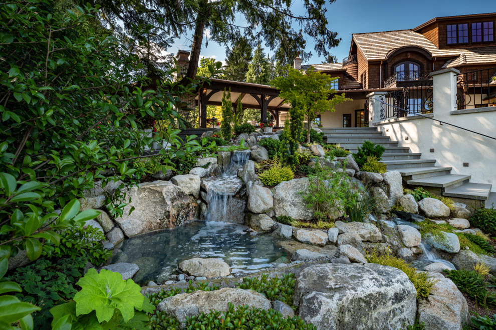 Foto di un ampio giardino tradizionale esposto a mezz'ombra dietro casa in estate con una cascata e sassi di fiume