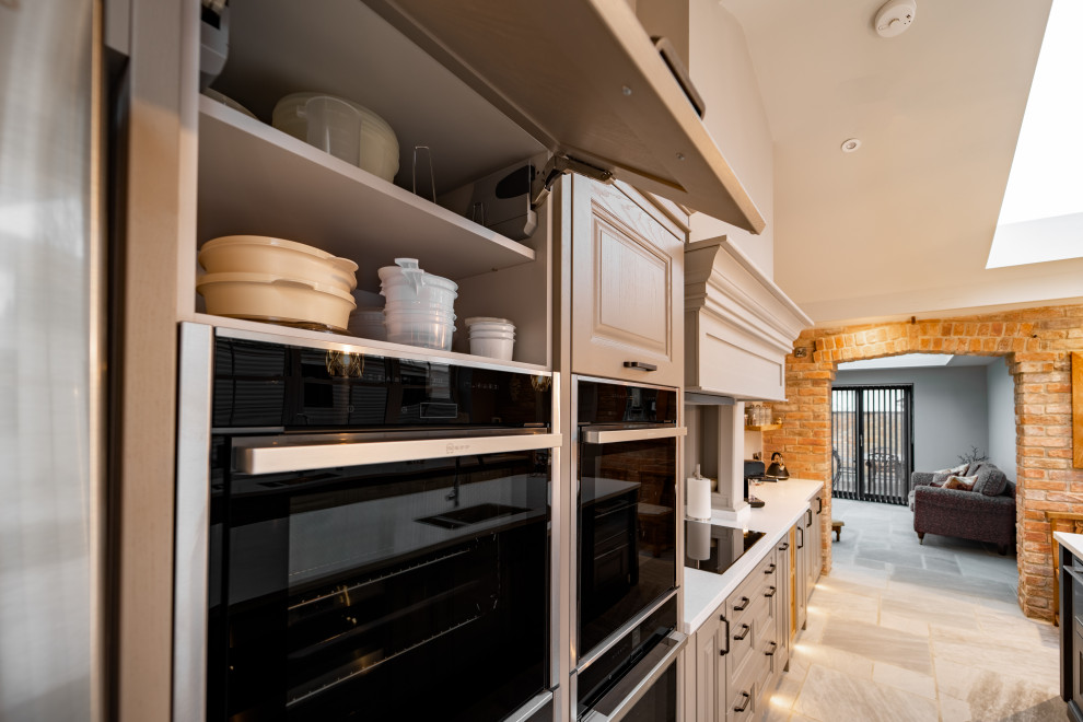 This is an example of a large classic galley open plan kitchen in Other with an integrated sink, raised-panel cabinets, grey cabinets, composite countertops, white splashback, black appliances, ceramic flooring, an island, grey floors, white worktops and a vaulted ceiling.