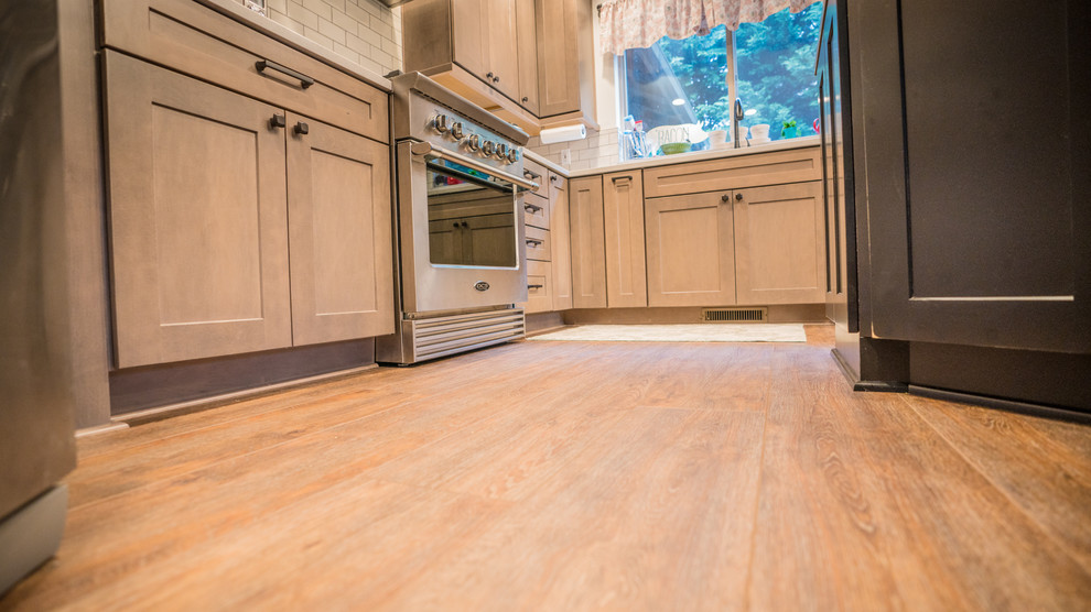 Large transitional l-shaped vinyl floor and brown floor open concept kitchen photo in Seattle with an undermount sink, recessed-panel cabinets, medium tone wood cabinets, quartz countertops, white backsplash, subway tile backsplash, stainless steel appliances, an island and white countertops