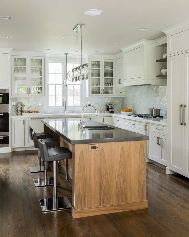 Photo of a mid-sized traditional l-shaped kitchen in Boston with white cabinets, white splashback, dark hardwood floors, with island, an undermount sink, shaker cabinets, solid surface benchtops, stone tile splashback, panelled appliances and brown floor.