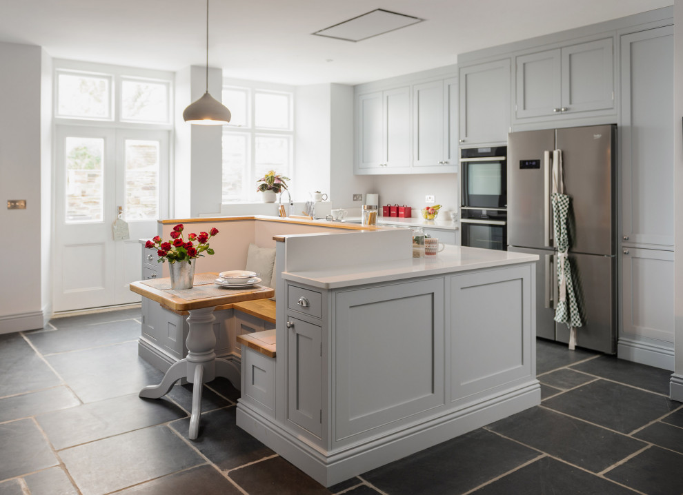 Photo of a large country u-shaped open plan kitchen in Cornwall with a drop-in sink, shaker cabinets, grey cabinets, quartzite benchtops, white splashback, black appliances, limestone floors, with island, black floor and white benchtop.
