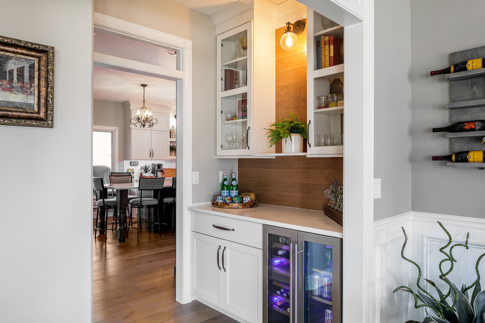 Eat-in kitchen - u-shaped brown floor eat-in kitchen idea with shaker cabinets, white cabinets, quartz countertops, white backsplash, subway tile backsplash, stainless steel appliances, an island, white countertops and a farmhouse sink