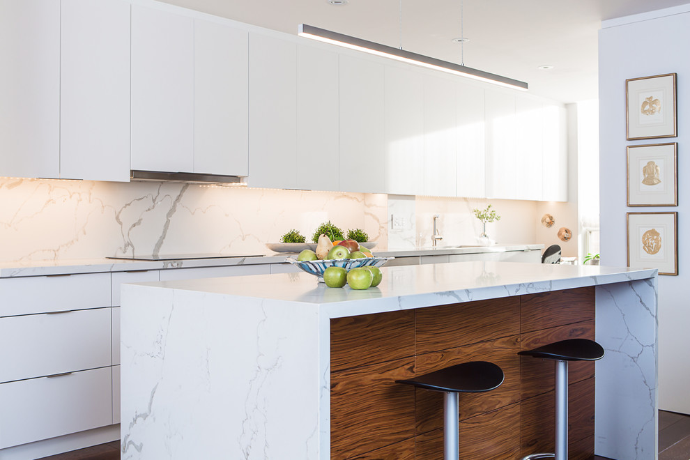 Photo of a mid-sized contemporary galley separate kitchen in Toronto with an undermount sink, flat-panel cabinets, white cabinets, quartz benchtops, white splashback, stone slab splashback, stainless steel appliances, medium hardwood floors, with island and brown floor.