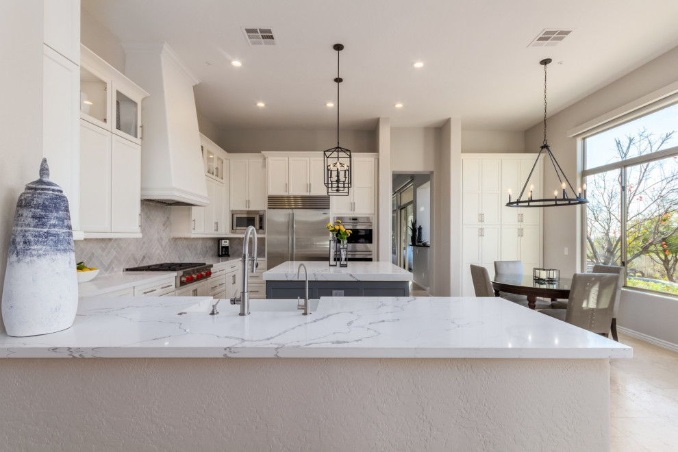 Eat-in kitchen - large transitional u-shaped travertine floor and beige floor eat-in kitchen idea in Phoenix with a farmhouse sink, shaker cabinets, white cabinets, quartz countertops, gray backsplash, ceramic backsplash, stainless steel appliances, an island and white countertops