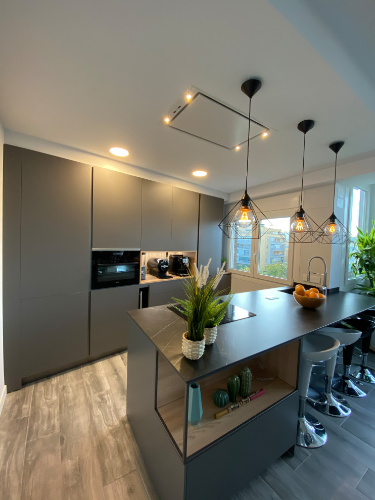 Ejemplo de cocina lineal contemporánea de tamaño medio abierta con fregadero bajoencimera, armarios con paneles lisos, puertas de armario negras, encimera de cuarzo compacto, electrodomésticos negros, suelo laminado, una isla, suelo marrón y encimeras negras