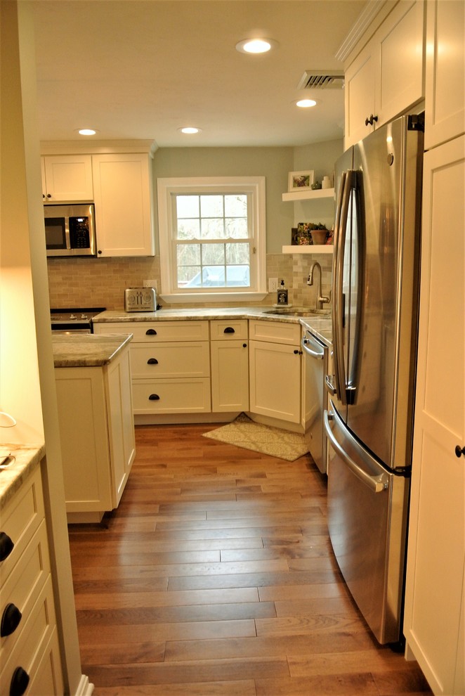 Inspiration for a transitional l-shaped medium tone wood floor kitchen remodel in Boston with an undermount sink, shaker cabinets, white cabinets, granite countertops, beige backsplash, subway tile backsplash, stainless steel appliances and an island