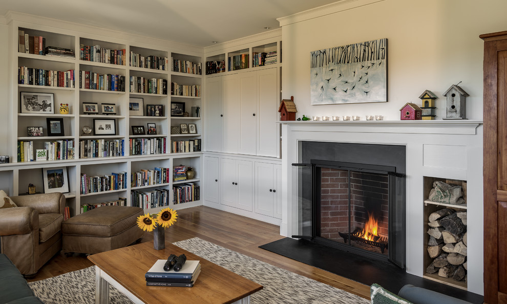 Inspiration for a mid-sized traditional open concept living room in Portland Maine with a library, white walls, medium hardwood floors, a standard fireplace, a stone fireplace surround and a concealed tv.