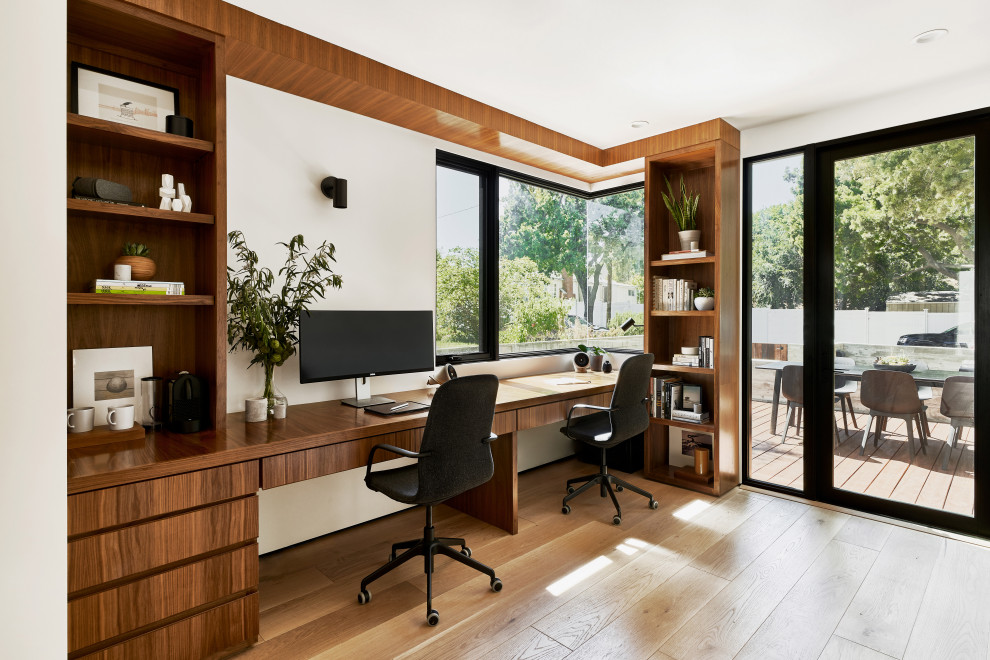 This is an example of a mid-sized contemporary study room in Los Angeles with white walls, medium hardwood floors, no fireplace, a built-in desk and brown floor.