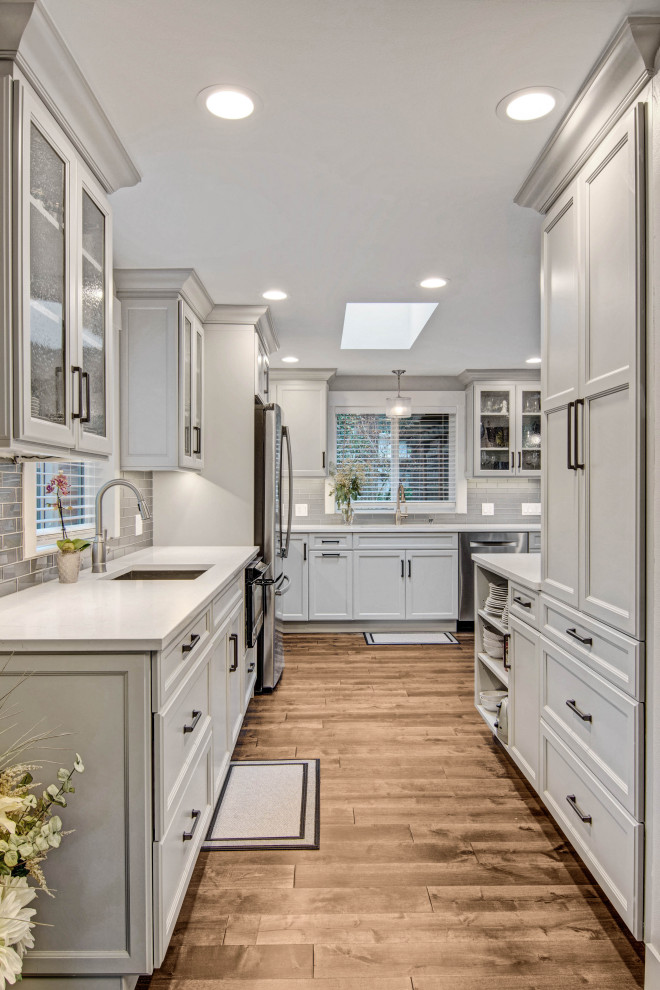 Inspiration for a transitional medium tone wood floor and brown floor open concept kitchen remodel in Seattle with an undermount sink, recessed-panel cabinets, gray cabinets, quartz countertops, gray backsplash, subway tile backsplash, stainless steel appliances, white countertops and a peninsula