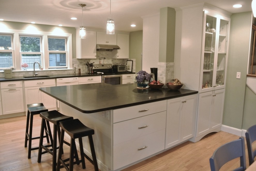 Example of a transitional u-shaped light wood floor eat-in kitchen design in Boston with an undermount sink, shaker cabinets, white cabinets, beige backsplash, porcelain backsplash, stainless steel appliances, a peninsula and black countertops