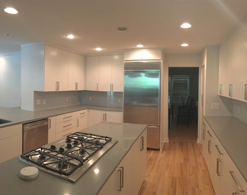 Example of a large transitional u-shaped light wood floor kitchen design in Dallas with an undermount sink, flat-panel cabinets, white cabinets, quartz countertops, gray backsplash, glass tile backsplash, stainless steel appliances and an island