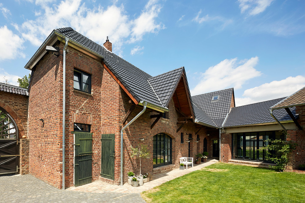 This is an example of a large country two-storey brick red house exterior in Cologne with a hip roof and a tile roof.