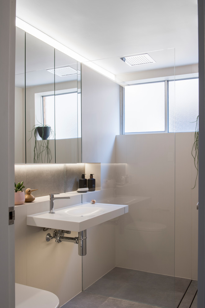 Photo of a small contemporary master bathroom in Sydney with an open shower, a wall-mount toilet, beige tile, cement tile, white walls, cement tiles, a wall-mount sink, solid surface benchtops, grey floor and an open shower.