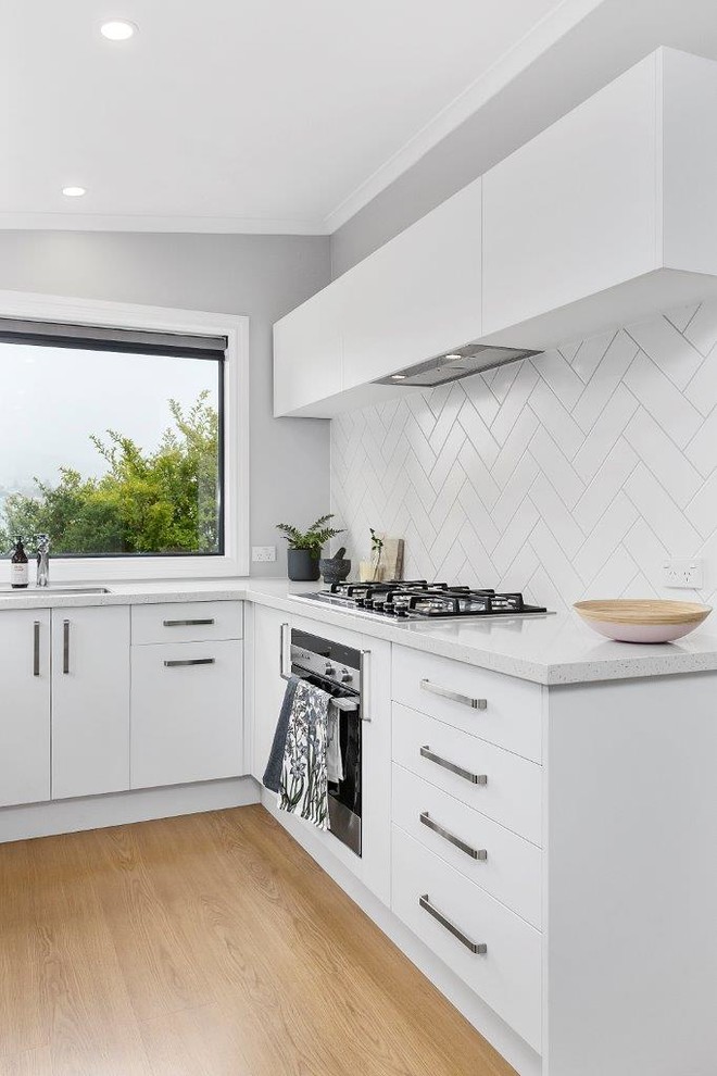 This is an example of a scandinavian u-shaped kitchen in Other with a drop-in sink, white cabinets, white splashback, ceramic splashback, stainless steel appliances, laminate floors and brown floor.