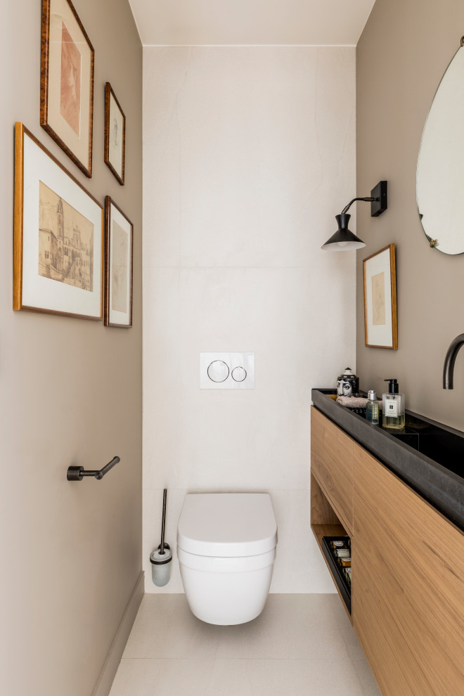 This is an example of a small contemporary cloakroom in Paris with beaded cabinets, medium wood cabinets, a wall mounted toilet, beige tiles, ceramic tiles, beige walls, ceramic flooring, a console sink, quartz worktops, beige floors, black worktops and a floating vanity unit.