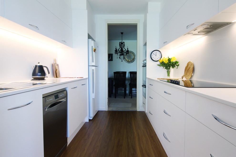 This is an example of a small modern galley separate kitchen in Sydney with a double-bowl sink, flat-panel cabinets, white cabinets, quartz benchtops, white splashback, stone slab splashback, stainless steel appliances, vinyl floors, no island, brown floor and white benchtop.