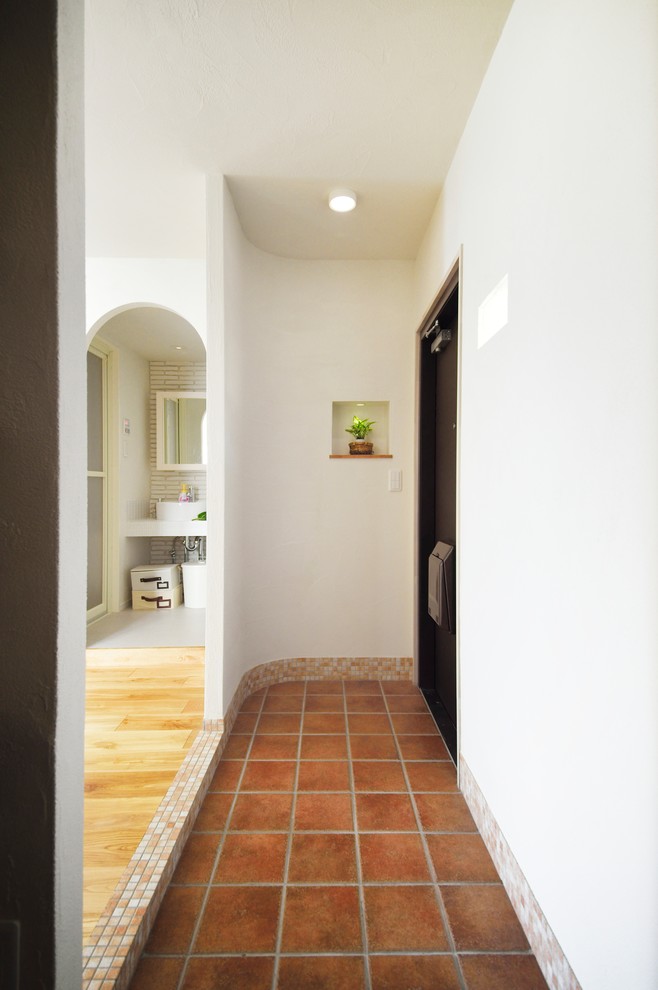 This is an example of a mediterranean entry hall in Other with white walls, terra-cotta floors, a single front door, a black front door and brown floor.