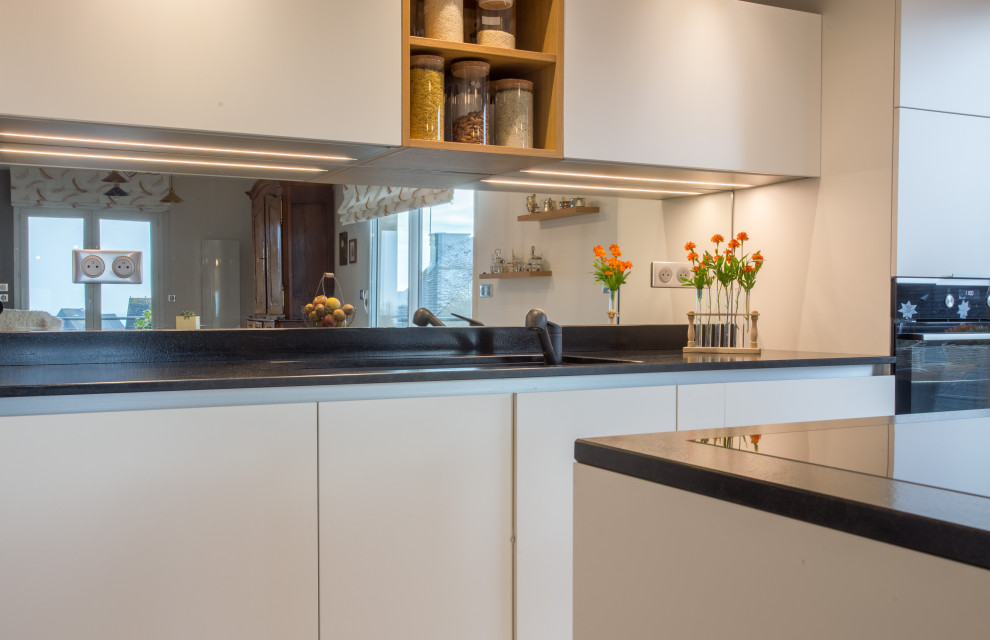 Photo of a mid-sized modern l-shaped open plan kitchen in Other with an integrated sink, beaded inset cabinets, white cabinets, granite benchtops, mirror splashback, stainless steel appliances, cement tiles, with island, multi-coloured floor and black benchtop.