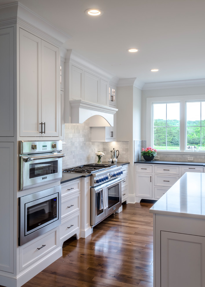 Photo of a large traditional kitchen in Cleveland with shaker cabinets, grey splashback, subway tile splashback, stainless steel appliances, medium hardwood floors, with island, brown floor, an undermount sink and white cabinets.