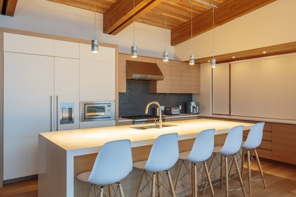 Inspiration for a mid-sized contemporary l-shaped open plan kitchen in Calgary with a double-bowl sink, flat-panel cabinets, light wood cabinets, solid surface benchtops, grey splashback, glass tile splashback, panelled appliances, light hardwood floors, with island and brown floor.