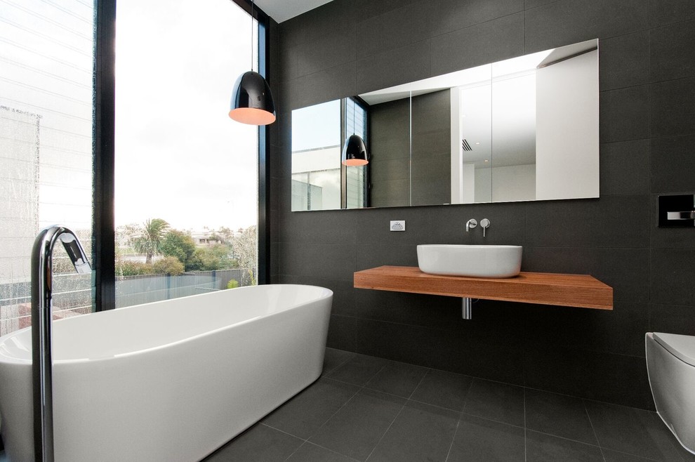 Mid-sized contemporary master bathroom in Adelaide with medium wood cabinets, a freestanding tub, a one-piece toilet, black tile, cement tile, black walls, cement tiles, a vessel sink, wood benchtops, black floor and an open shower.