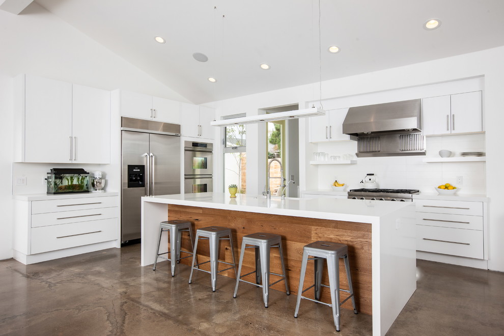 Mid-sized contemporary l-shaped kitchen in Orange County with white cabinets, quartz benchtops, stainless steel appliances, flat-panel cabinets, white splashback, concrete floors, with island and brown floor.
