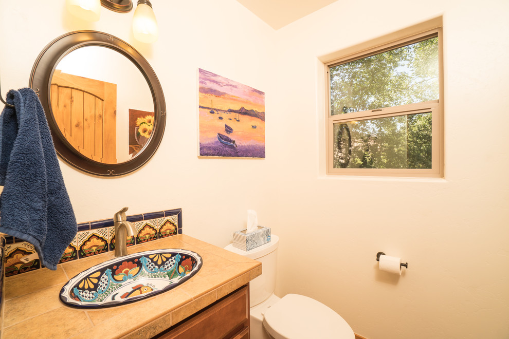 Photo of a mid-sized powder room in Other with raised-panel cabinets, medium wood cabinets, multi-coloured tile, beige walls, tile benchtops, beige benchtops, a one-piece toilet, terra-cotta tile, ceramic floors, a drop-in sink, beige floor and a built-in vanity.