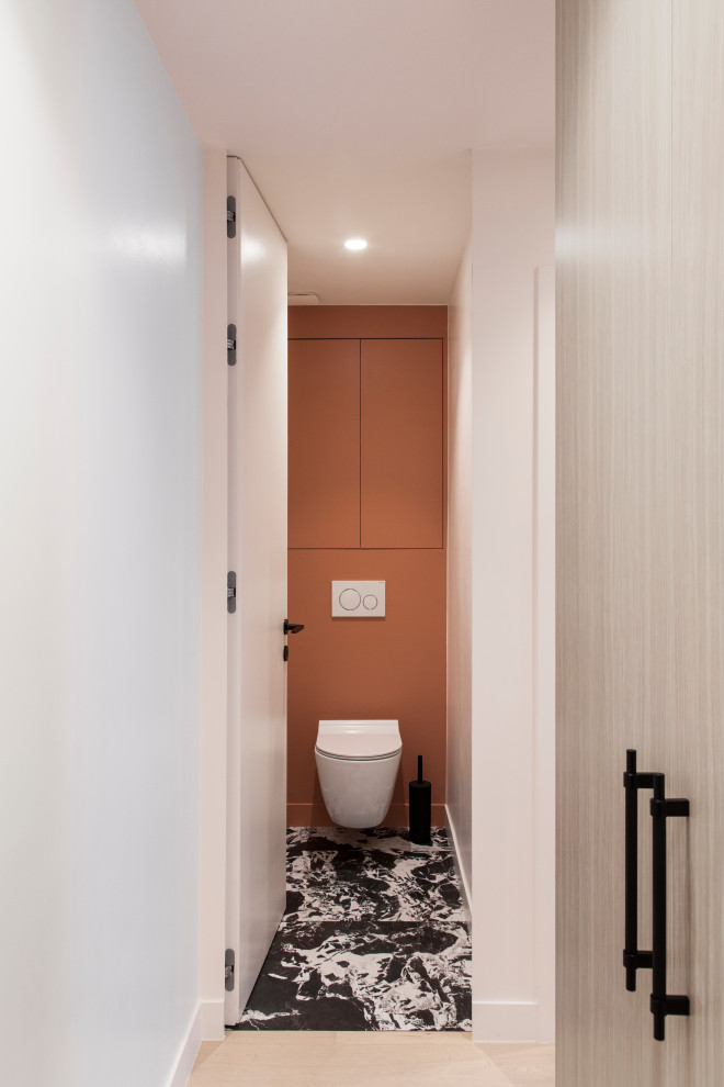 Bild på ett mellanstort funkis toalett, med luckor med profilerade fronter, orange skåp, en vägghängd toalettstol, orange väggar, marmorgolv och svart golv