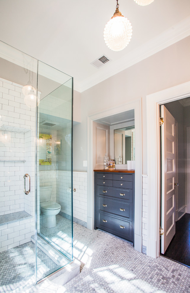 This is an example of a mid-sized transitional master bathroom in DC Metro with a corner shower, furniture-like cabinets, blue cabinets, wood benchtops, a one-piece toilet, white tile, subway tile, white walls and ceramic floors.