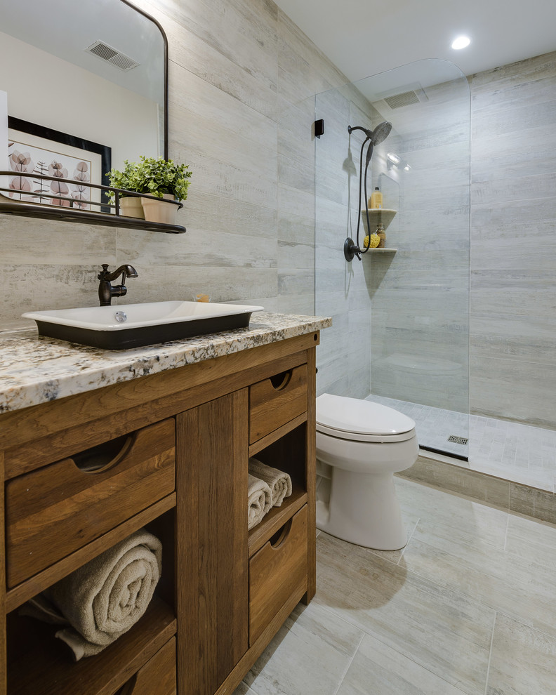 Inspiration for a mid-sized country 3/4 bathroom in Baltimore with furniture-like cabinets, medium wood cabinets, an open shower, a two-piece toilet, gray tile, porcelain tile, beige walls, porcelain floors, a vessel sink, granite benchtops, grey floor, an open shower and multi-coloured benchtops.