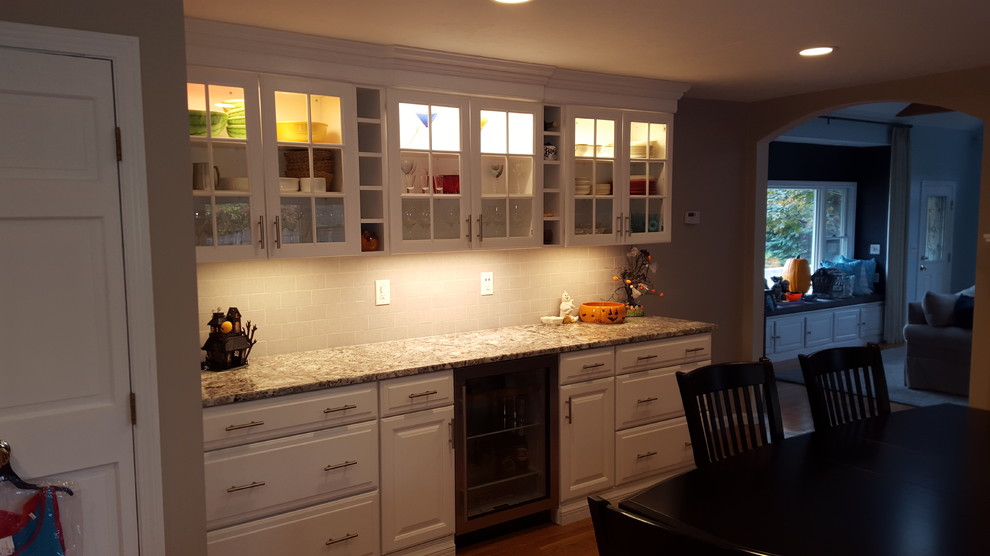 Large transitional l-shaped light wood floor eat-in kitchen photo in Boston with an undermount sink, raised-panel cabinets, white cabinets, granite countertops, gray backsplash, ceramic backsplash, stainless steel appliances and an island