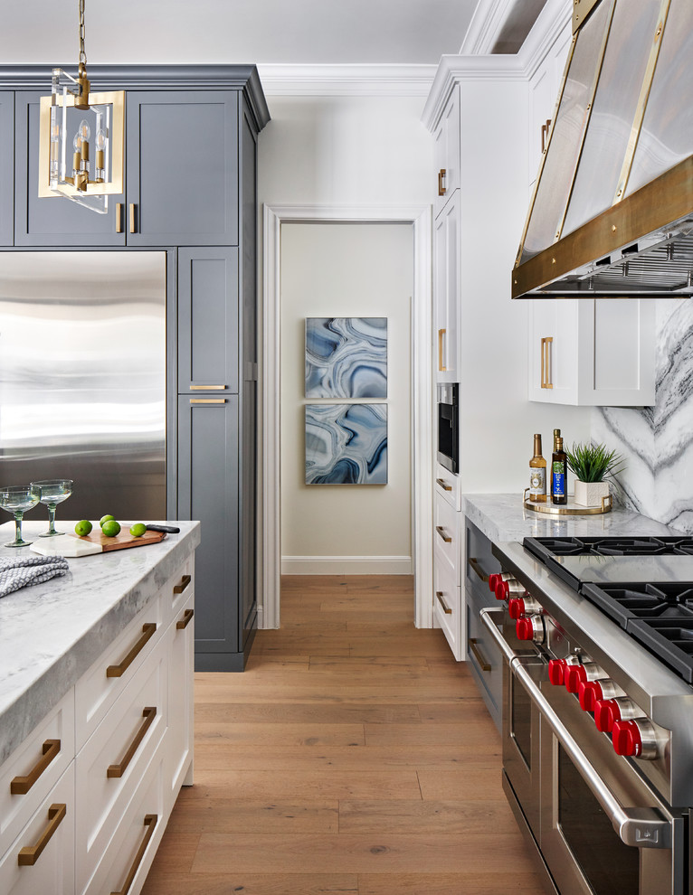 Photo of a mid-sized transitional l-shaped open plan kitchen in Austin with a farmhouse sink, shaker cabinets, grey cabinets, quartzite benchtops, multi-coloured splashback, marble splashback, stainless steel appliances, light hardwood floors, multiple islands, grey floor and blue benchtop.