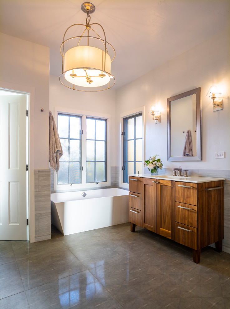 This is an example of a medium sized contemporary ensuite bathroom in Denver with recessed-panel cabinets, medium wood cabinets, a freestanding bath, a built-in shower, green tiles, porcelain tiles, white walls, porcelain flooring, a submerged sink, engineered stone worktops, grey floors, a hinged door, white worktops, a single sink, a freestanding vanity unit and wainscoting.