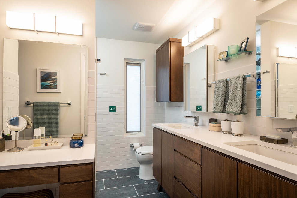 Photo of a mid-sized modern master bathroom in Indianapolis with flat-panel cabinets, medium wood cabinets, an alcove shower, a one-piece toilet, white tile, subway tile, white walls, porcelain floors, an undermount sink, engineered quartz benchtops, grey floor, a hinged shower door, white benchtops, a shower seat, a double vanity and a floating vanity.
