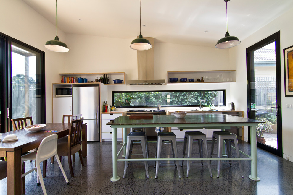 This is an example of a large industrial galley eat-in kitchen in Melbourne with a double-bowl sink, flat-panel cabinets, white cabinets, wood benchtops, white splashback, glass sheet splashback, stainless steel appliances, concrete floors and with island.